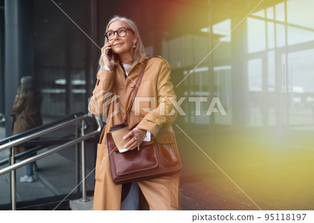 elderly stylish woman talking on mobile phone next to mall 95118197