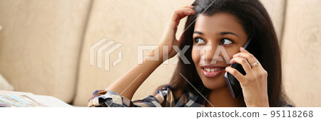 A dark-skinned girl on the floor house speaks on a phone 95118268