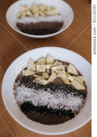Vegan raw flaxeed porridge with fruits and chia, black sesame and psyllium seeds, coconut flakes. Healthy nutritious and fresh food. Two plates Vegan raw flaxeed porridge with fruits and chia, black sesame and psyllium seeds, coconut flakes. Healthy nutritious and fresh food. Two plates 95118395
