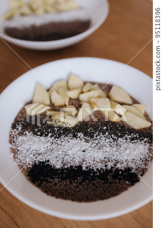 Vegan raw flaxeed porridge with fruits and chia, black sesame and psyllium seeds, coconut flakes. Healthy nutritious and fresh food. Two plates Vegan raw flaxeed porridge with fruits and chia, black sesame and psyllium seeds, coconut flakes. Healthy nutritious and fresh food. Two plates 95118396