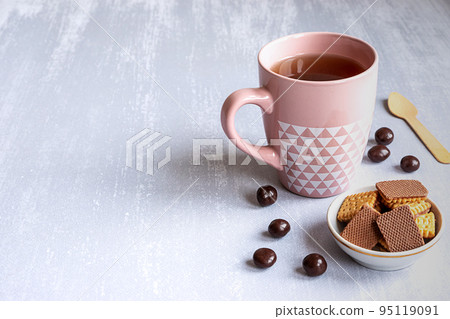 Pink cup of black tea on grey background, with cookies, chocolates and a wooden spoon. Copy space. Pink cup of black tea on grey background, with cookies, chocolates and a wooden spoon. Copy space. 95119091