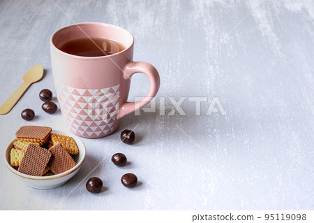 Pink cup of black tea on grey background, with cookies, chocolates and a wooden spoon. Copy space.  95119098