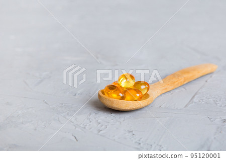 Vitamin omega capsules in a spoon on a colored background. Pills served as a healthy meal. Red soft gel vitamin supplement capsules on spoon 95120001