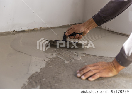 Grey self-leveling screed, new floor layer, man hand. 95120289