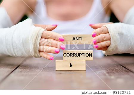 The text anti corruption is laid out by a woman with wooden blocks with her hands in casts 95120751