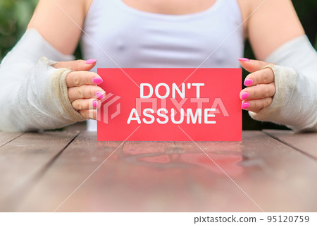 DO NOT ASSUME the text on the red card in the hands of a woman with casts on her hands DO NOT ASSUME the text on the red card in the hands of a woman with casts on her hands 95120759