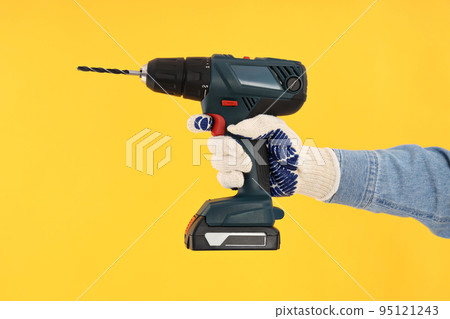 Hand in glove holds drill on yellow background Hand in glove holds drill on yellow background 95121243