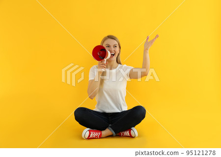 Young woman with megaphone on yellow background 95121278