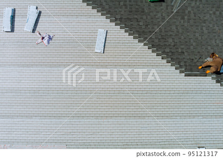 Worker nailed new roof shingles bitumen using air hammer an aerial top view Worker nailed new roof shingles bitumen using air hammer an aerial top view 95121317