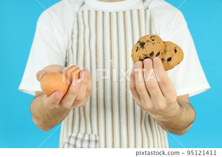 Young man holds cookies and eggs on blue background 95121411