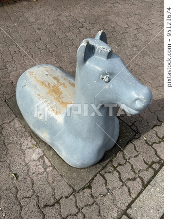 Retro playground equipment in a park: A fixed horse-shaped play structure with slightly peeling paint creates a nostalgic scene. 95121674
