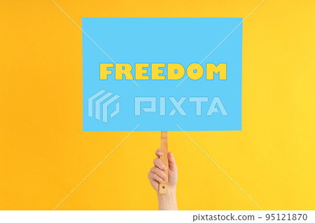 Female hand holds protest sign with text Freedom on yellow background 95121870
