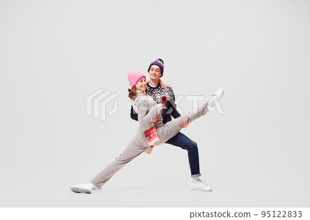 Cute young couple of ballet dancers in warm winter sportswear drinking tea or mulled wine isolated on gray background. Retro, vintage, dance, holidays, party concept 95122833