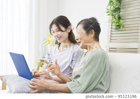 Grandson and grandmother using a computer in the living room Grandson and grandmother using a computer in the living room 95123196
