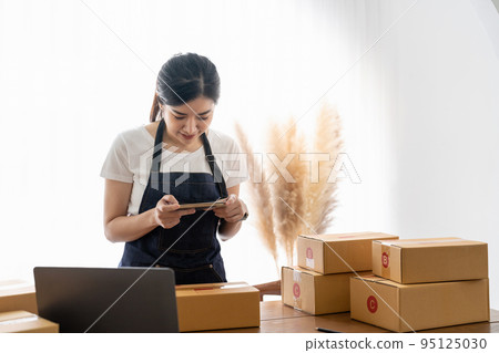 Woman taking photo to cardboard box with smartphone for post to sell online on the Internet and preparing pack product box. Selling online ideas concept 95125030