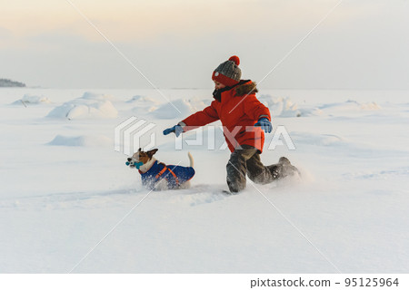 On pleasant winter day kid chasing family pet dog in deep snow On pleasant winter day kid chasing family pet dog in deep snow 95125964