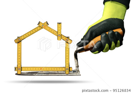 Gloved Hand Holding a Trowel and Folding Ruler in the Shape of House 95126834