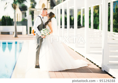 Beautiful bride and groom embracing and kissing on their wedding day 95129288