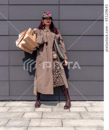 A happy shopaholic girl keeps her bags near the shopping center. A woman near the store is happy with her purchases, holding bags. Dressed in a leopard print dress. Consumer concept. A happy shopaholic girl keeps her bags near the shopping center. A woman near the store is happy with her purchases, holding bags. Dressed in a leopard print dress. Consumer concept. 95129643