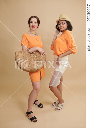 Portrait of beautiful models demonstrating fashion summer clothes against orange background 95130027