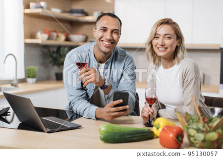 Multiracial couple using smartphone while having breakfast at kitchen Multiracial couple using smartphone while having breakfast at kitchen 95130057
