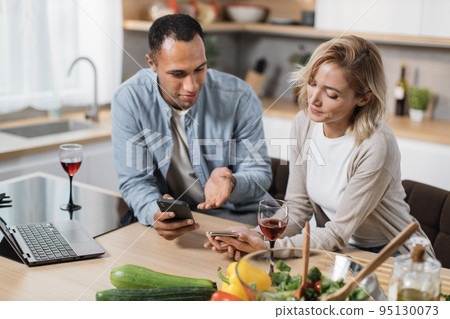 Close up view of multinational couple using cell phone while having breakfast at kitchen Close up view of multinational couple using cell phone while having breakfast at kitchen 95130073