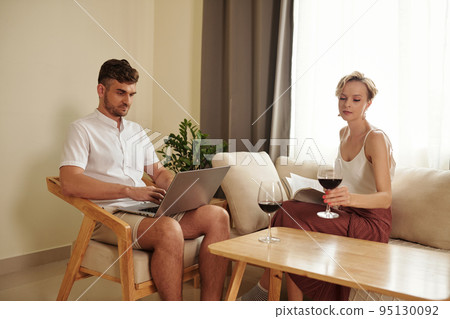 Young couple sitting in living room, drinking red wine and using laptop at home Young couple sitting in living room, drinking red wine and using laptop at home 95130092
