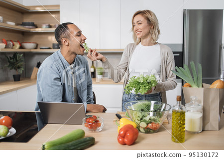 Blond young wife spouses having fun while feeding her husband with lettuce salad Blond young wife spouses having fun while feeding her husband with lettuce salad 95130172