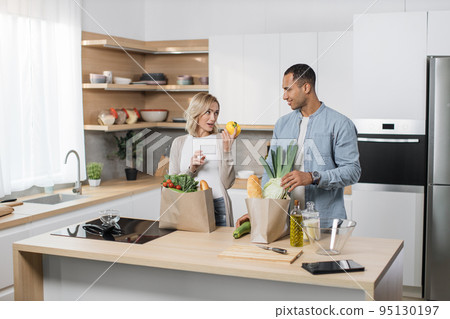 Positive young people in love unpacking shopping back with fresh organic products. Positive young people in love unpacking shopping back with fresh organic products. 95130197