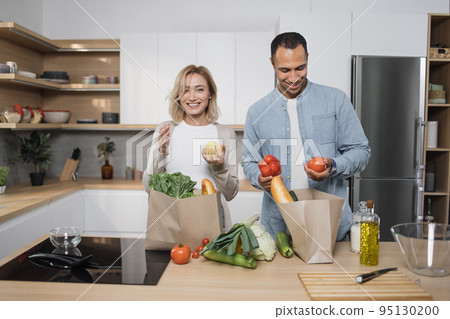 Positive young people in love unpacking shopping back with fresh organic products. Positive young people in love unpacking shopping back with fresh organic products. 95130200