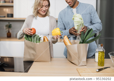Cropped image of married couple coming home from shopping and unpacking paper bags with groceries Cropped image of married couple coming home from shopping and unpacking paper bags with groceries 95130202