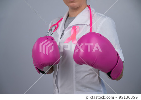 Faceless female doctor in pink boxing gloves with a pink ribbon on a gray background. Fight against breast cancer.  95130359