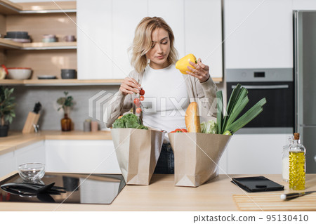 Attractive female unpacking paper bag with fresh products. Attractive female unpacking paper bag with fresh products. 95130410