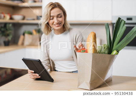 Focus on hand holding tablet and paper bag with vegetables. Focus on hand holding tablet and paper bag with vegetables. 95130438