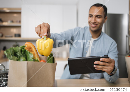 Focus on hand of blurred indian man in kitchen taking yellow pepper from grocery shopping bag 95130474