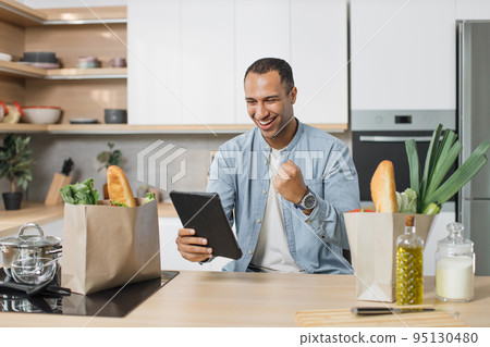 Joyful excited arabian man chef cooking, rejoices to found a favorite recipe on digital tablet 95130480