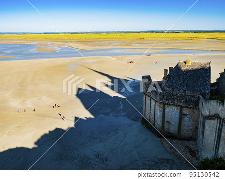 Le Mont Saint Michel, impressive shadow of the famous abbey and tourists walking on the colourful sand flats during low tide, Normandy, Northern France 95130542