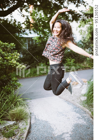 Young happy mixed race Japanese woman in jeans, shirt and sneakers in summer park, jumping and smiling Young happy mixed race Japanese woman in jeans, shirt and sneakers in summer park, jumping and smiling 95130552