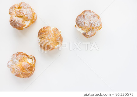 Choux Bun with whipped cream and sugar powder on top on white background. Delicate choux pastry dessert. French cream puff. Top view, copy space Choux Bun with whipped cream and sugar powder on top on white background. Delicate choux pastry dessert. French cream puff. Top view, copy space 95130575