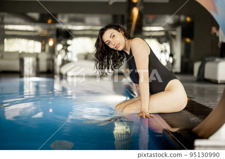 Woman rests by the swimming pool indoors at spa resort Woman rests by the swimming pool indoors at spa resort 95130990