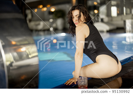 Woman rests by the swimming pool indoors at spa resort 95130992