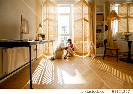Woman sits with dog by the window blinds at home Woman sits with dog by the window blinds at home 95131267
