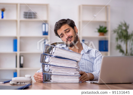 Young male employee unhappy with excessive work in the office Young male employee unhappy with excessive work in the office 95131645