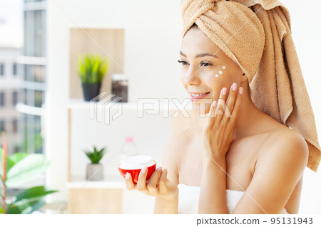 Beautiful woman applying moisturizer cream on her face. 95131943