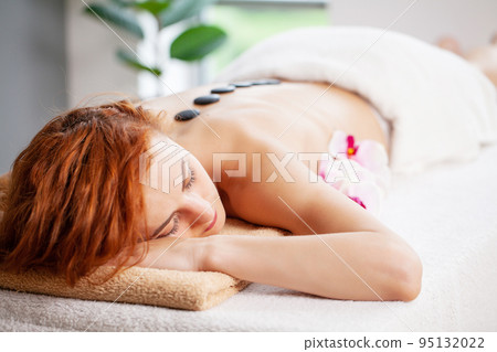 Beautiful woman relaxing in spa salon with hot stones on body. 95132022