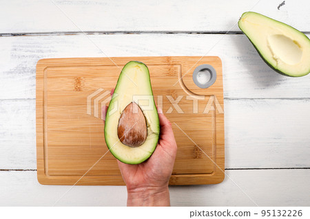 Avocado fruit in a woman's hand. Bamboo cutting board in background 95132226