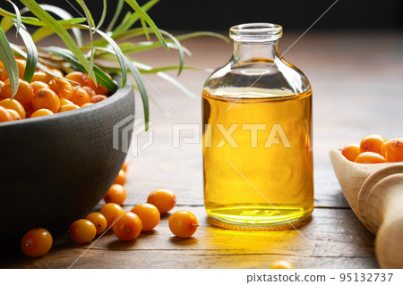 Bottle of sea buckthorn essential oil, bowl of sandthorn berries, wooden scoop of sea buckthorn berries. Bottle of sea buckthorn essential oil, bowl of sandthorn berries, wooden scoop of sea buckthorn berries. 95132737