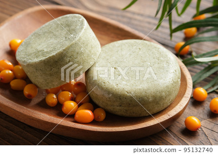 Solid shampoo pieces with sea buckthorn berries extract or homemade natural organic soap bars on wooden soap dish. Ripe sea buckthorn berries on wooden board. 95132740