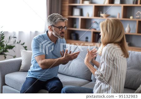Angry aggressive middle aged european male in glasses swears at female, freaking out in living room interior 95132983