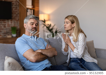Sad middle aged european woman asks man for forgiveness after quarrel in living room interior Sad middle aged european woman asks man for forgiveness after quarrel in living room interior 95132995